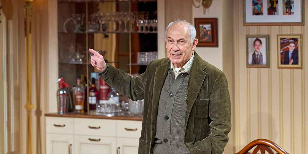 Nicholas Woodeson as David Rosenberg gestures while speaking in a warmly decorated interior setting.
