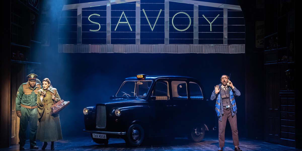 A vibrant scene from Paddington The Musical, featuring Paddington Bear in a red hat and blue coat.
