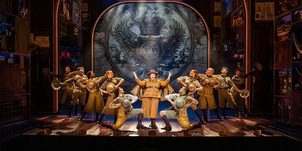 A scene from Paddington The Musical featuring a bear in a red hat and blue coat on stage.