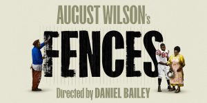 A close-up of a wooden fence with a weathered texture, surrounded by greenery and soft sunlight. In the centre it reads 'Fences'.