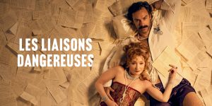 Two people lay together in dramatic costume, showcasing rich fabrics and textures against a background of sheets of paper.