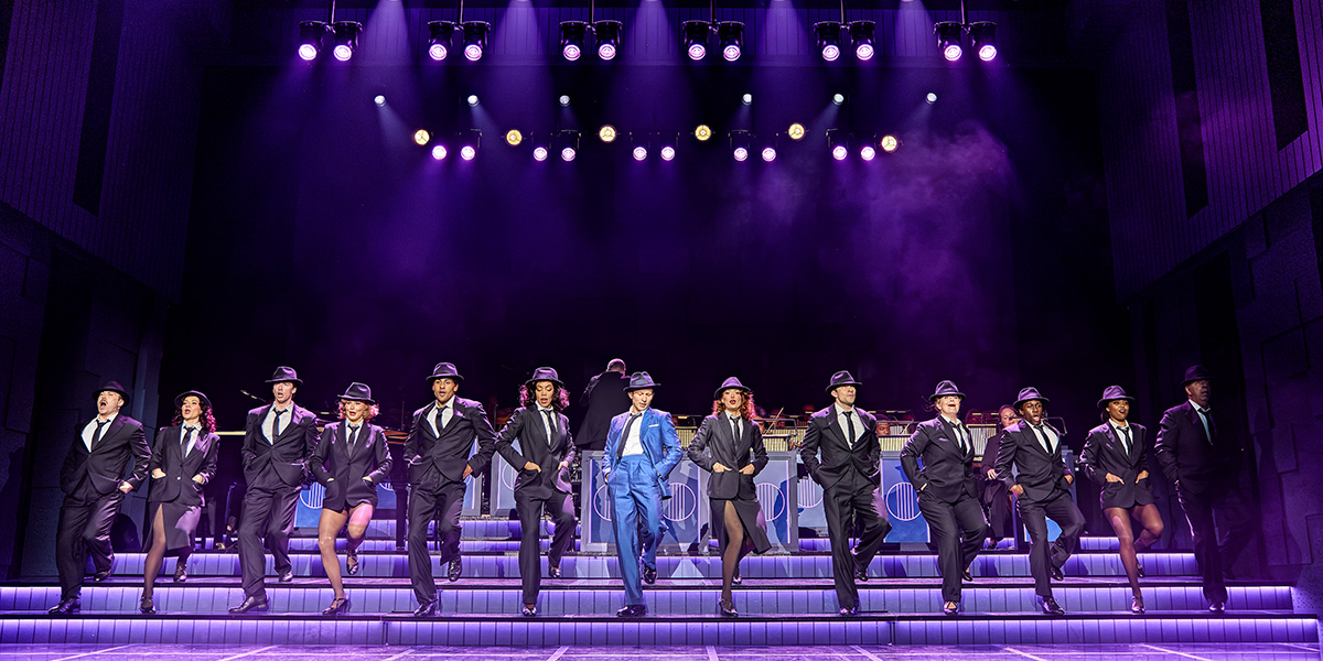 Joel Harper-Jackson performs centre stage in Sinatra The Musical, surrounded by the ensemble in elegant costumes.