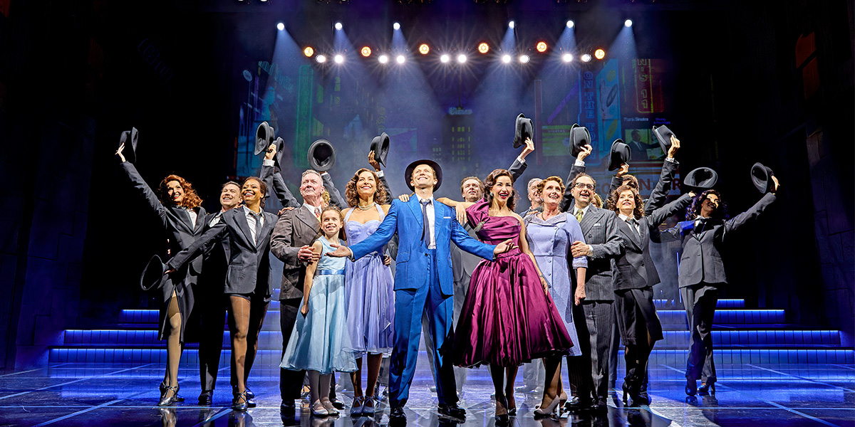 The entire cast of Sinatra The Musical poses together, wearing stylish costumes, with a vibrant stage backdrop.