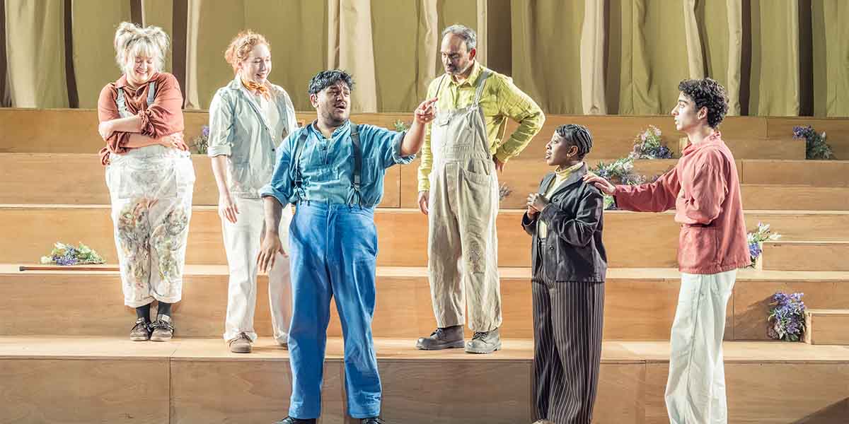 The cast of A Midsummer Night's Dream performs on stage, wearing colourful costumes and interacting expressively.