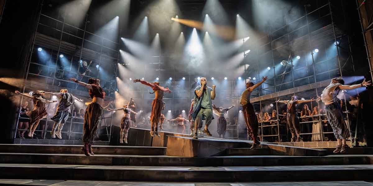 A dynamic musical performance featuring multiple dancers in dramatic poses, illuminated by bright stage lights.