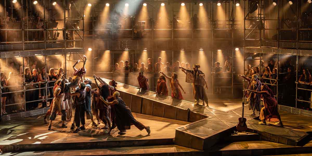 A dramatic scene from "Jesus Christ Superstar" featuring performers in vibrant costumes on a lit stage.