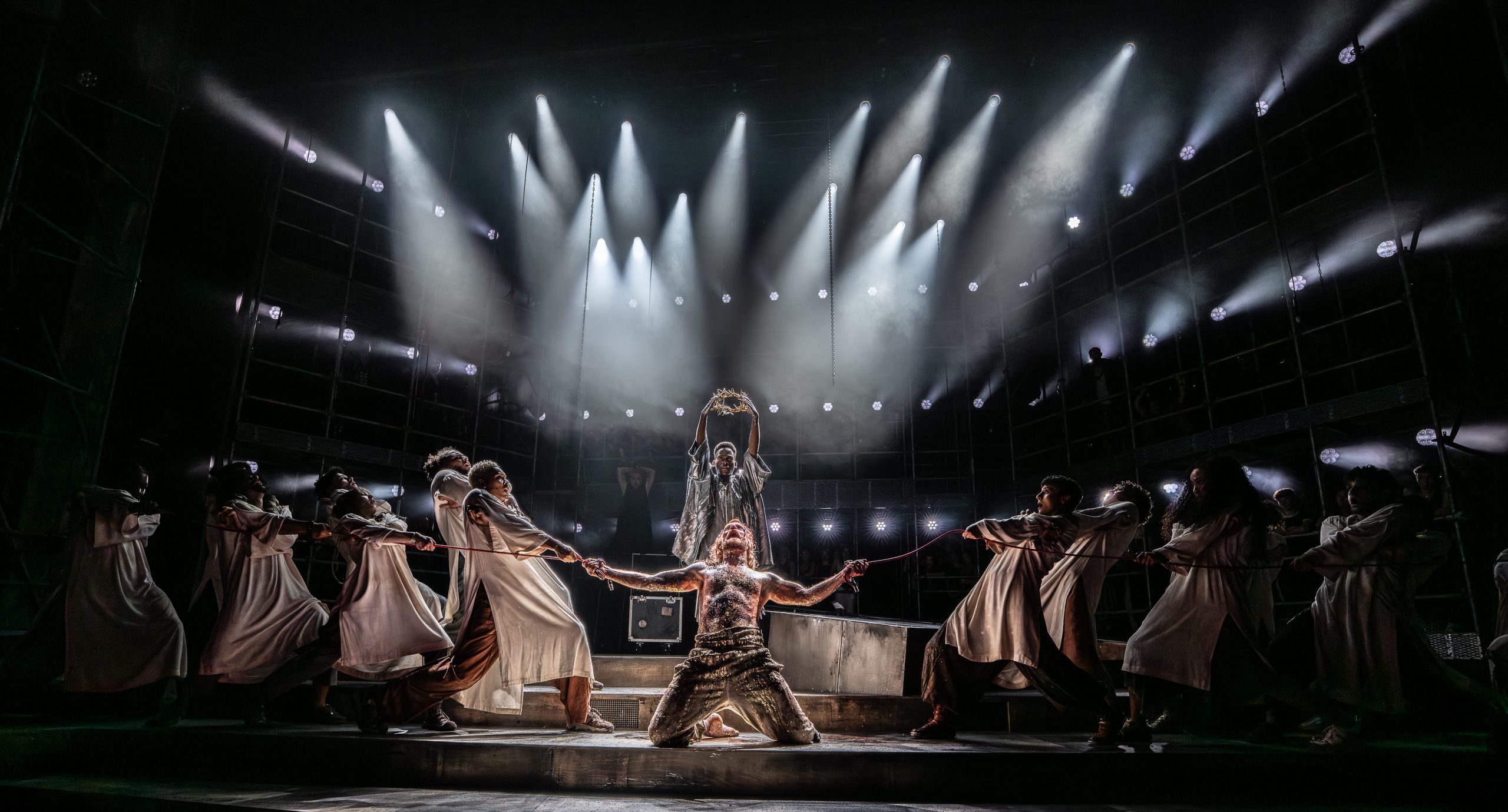 Sam Ryder performing on stage in a vibrant costume, surrounded by dramatic lighting and theatrical set design.
