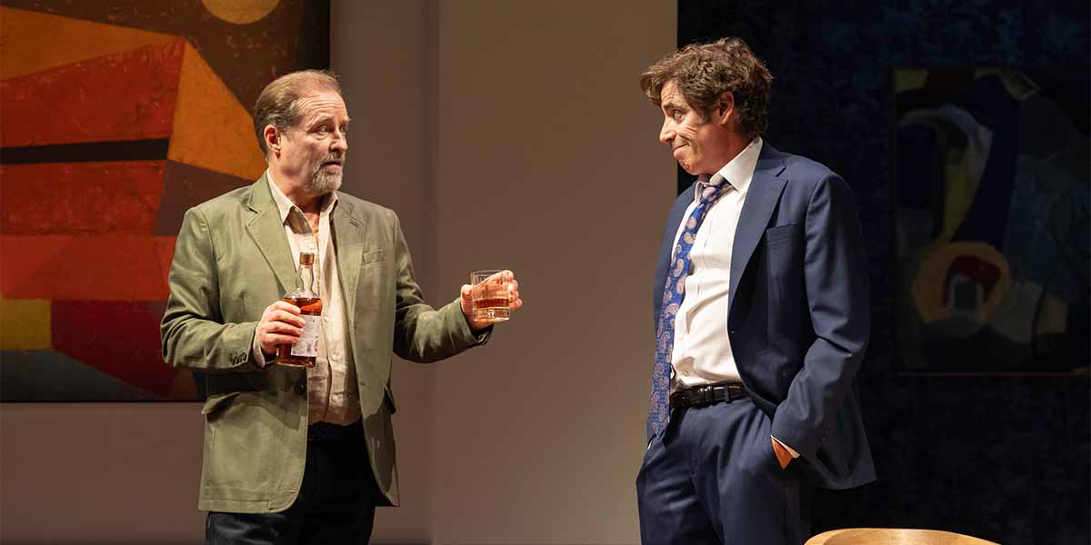 Two people engage in conversation, one holding a drink, against a backdrop of abstract artwork.