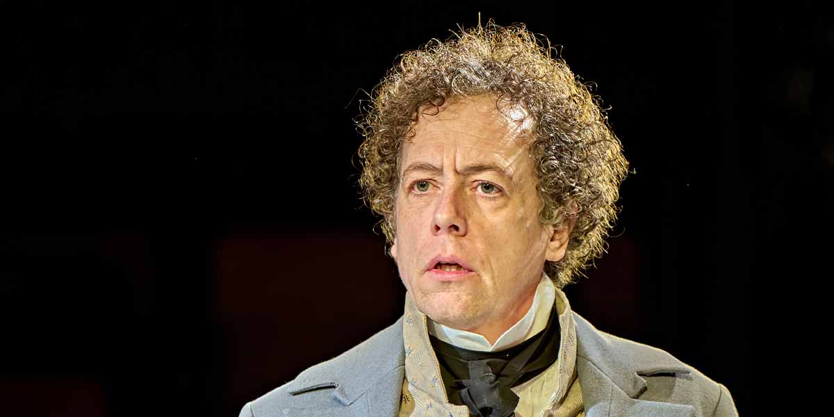 Matthew Steer as Ezra Chater, with curly hair and a serious expression, wearing a period costume.