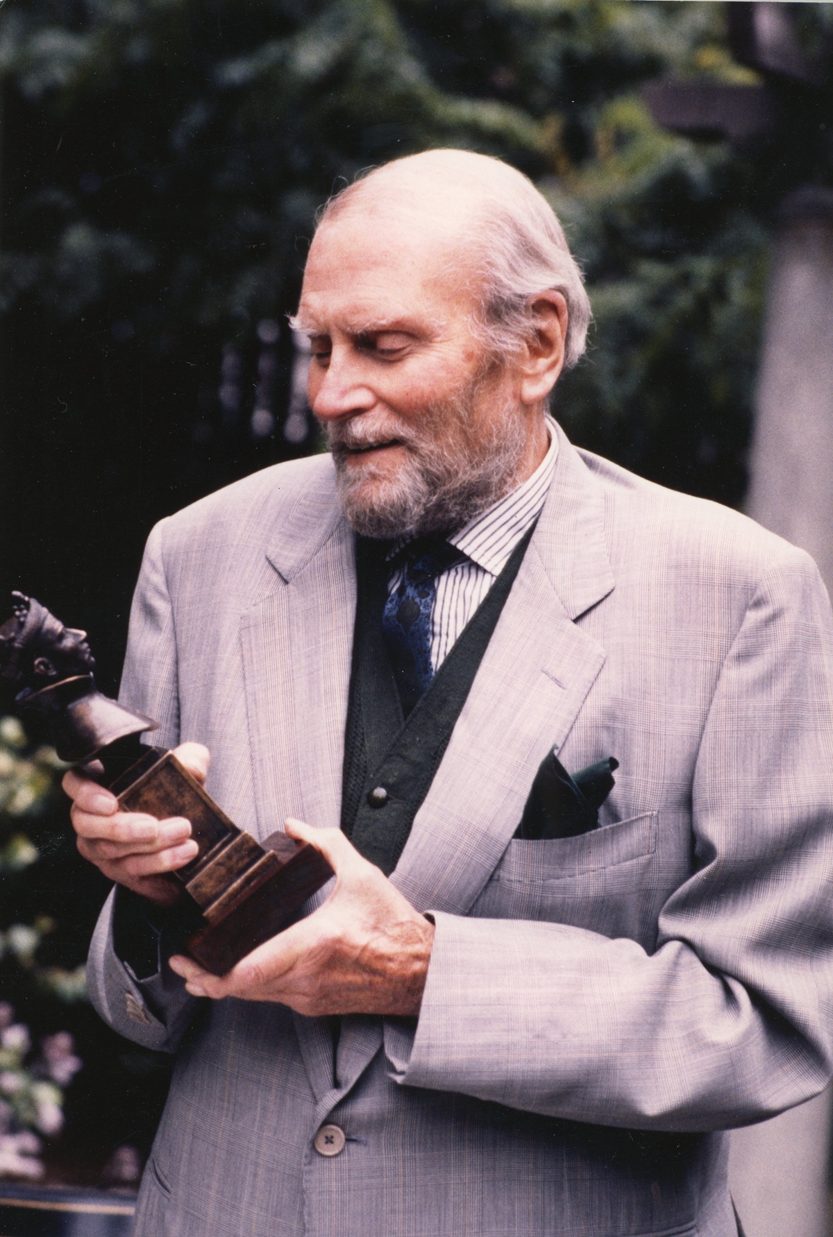 Laurence Olivier stands outside, holding an Olivier Award statue