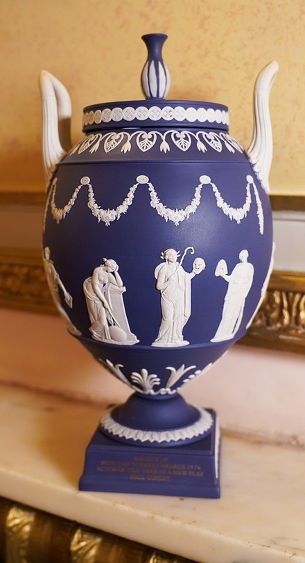A blue Wedgwood urn with white relief figures, featuring classical motifs and decorative handles, displayed on a marble surface.