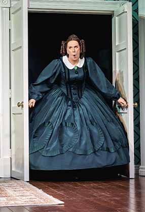 A woman in a dark green Victorian dress stands dramatically in an open doorway, expressing surprise.
