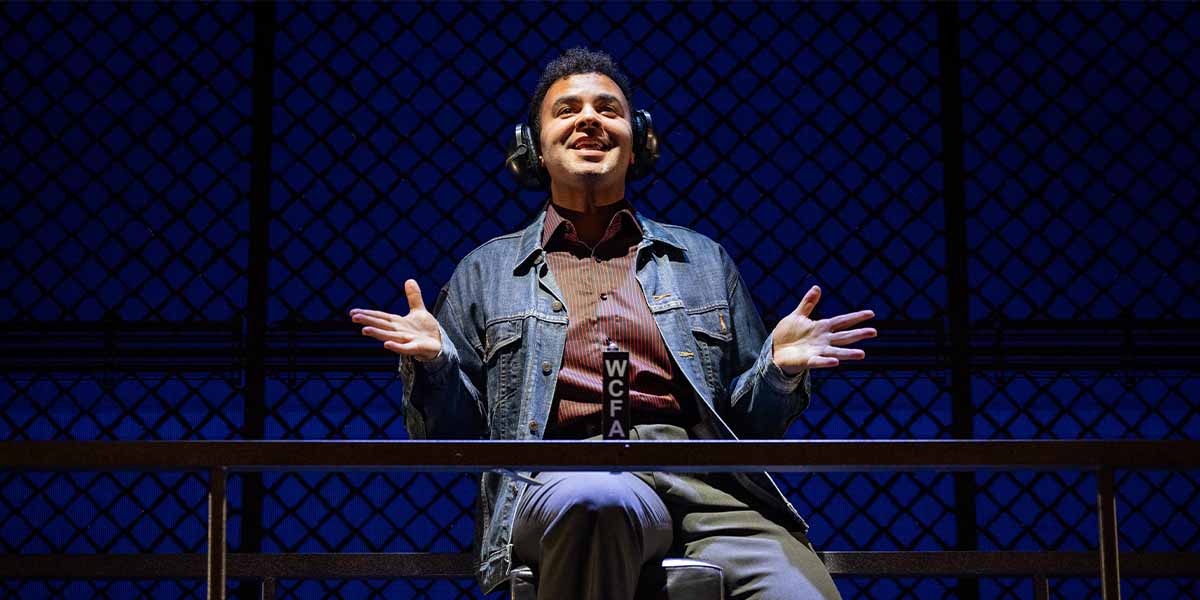 Damien Winchester as Barry Belson gestures while seated, wearing headphones against a blue backdrop.