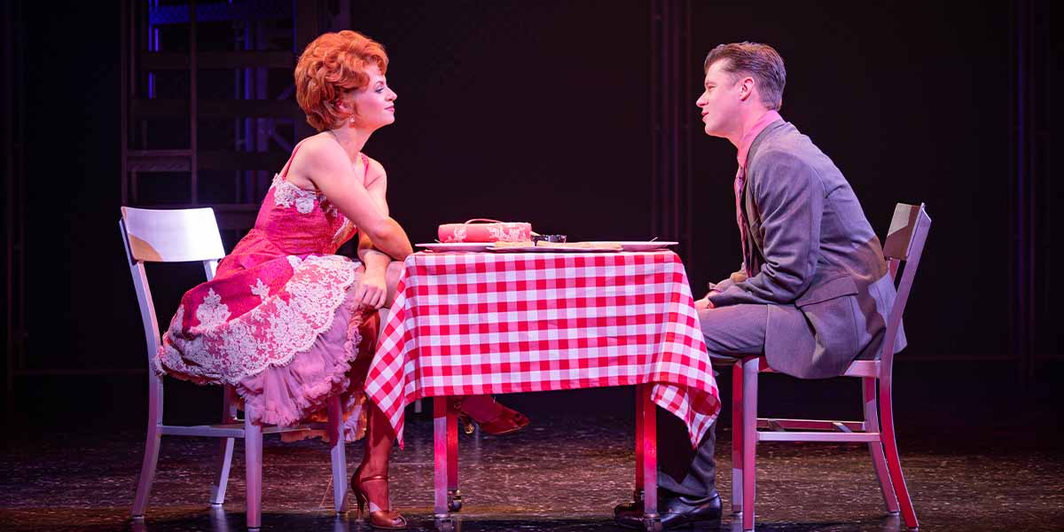 Sydnie Hocknell as Mary Delado and Luke Baker as Frankie Valli sit at a checkered table.