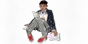 A young person sits cross-legged, reading a script, wearing a black jacket and red shoes.