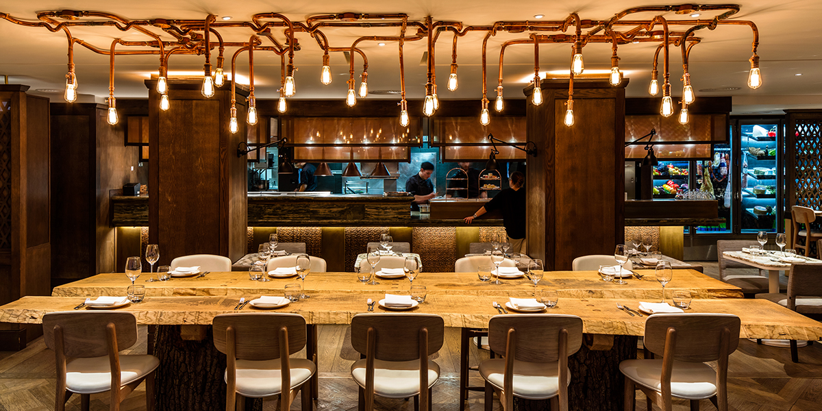 A stylish restaurant interior featuring wooden tables, plush seating, and elegant lighting fixtures.