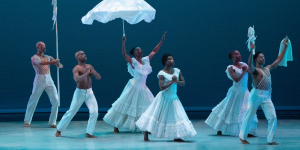 A vibrant dance performance featuring dancers in colourful costumes, showcasing dynamic movements against a dark background.