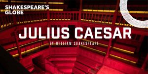 Interior of Shakespeare's Globe Theatre, featuring red lighting and text promoting "Julius Caesar" by William Shakespeare.