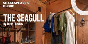 Costumes for "The Seagull" hang on a rack in a wooden room, with a spotlight and headphones visible.