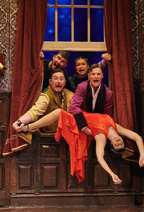 Four men in theatrical costumes peer out of a window, while a woman in a red dress hangs dramatically.